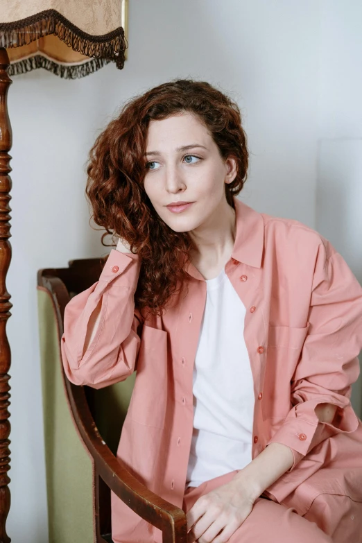 a woman sitting in a chair next to a lamp, a portrait, inspired by Anita Malfatti, trending on pexels, renaissance, cropped shirt with jacket, curly pink hair, coral brown hair, wearing a linen shirt