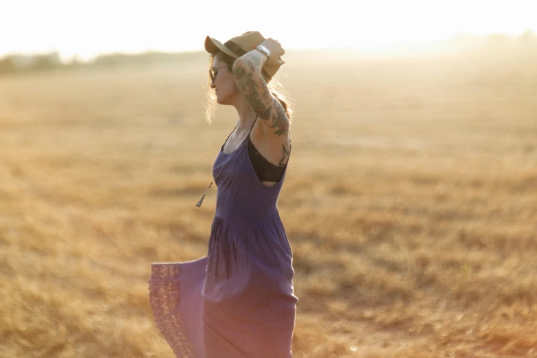 a woman in a purple dress standing in a field, by Jessie Algie, pexels, she is wearing a hat, sunny amber morning light, stubble, focus on full - body