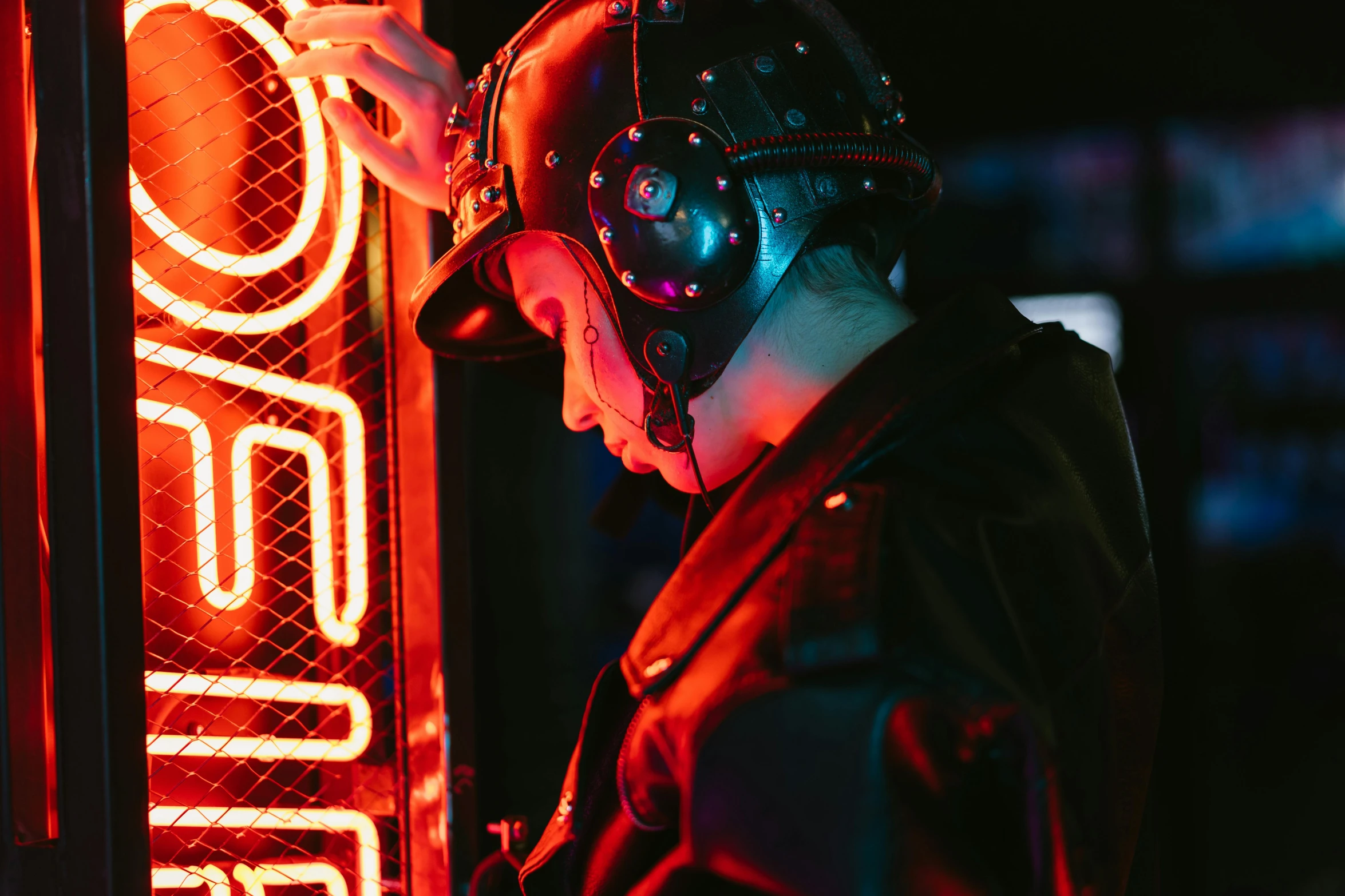 a man wearing a helmet standing next to a neon sign, cyberpunk art, unsplash, red and obsidian neon, headphones dj rave, dieselpunk atmosphere, photograph of a techwear woman