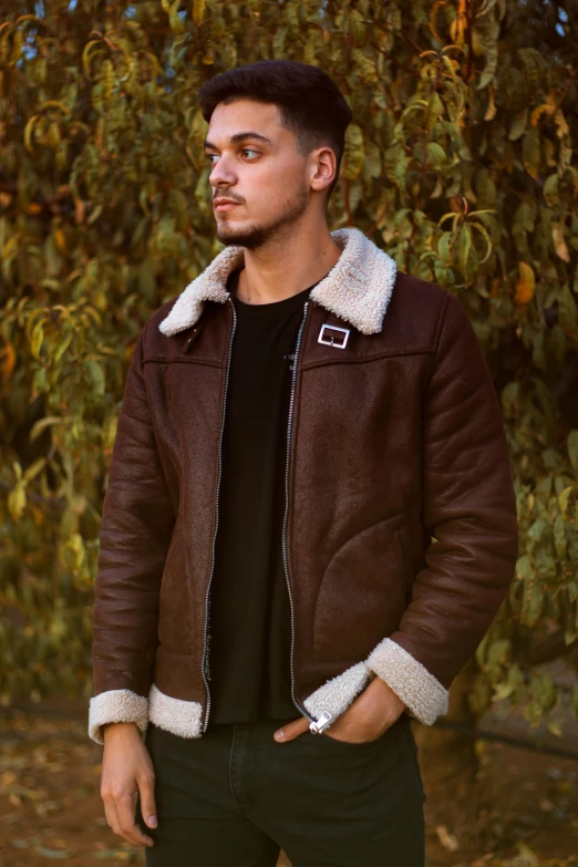 a man standing in front of a tree wearing a brown jacket, an album cover, by Julia Pishtar, pexels contest winner, wearing an aviator jacket, brown fur, thumbnail, male model