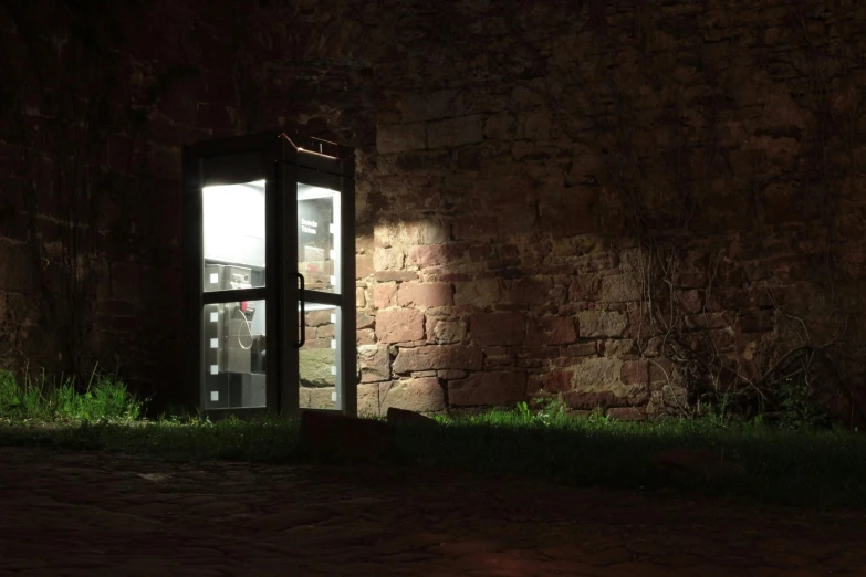 a phone booth sitting in front of a brick wall, by Attila Meszlenyi, pexels contest winner, night time render, inner ward of a medieval castle, outdoor art installation, medium format. soft light