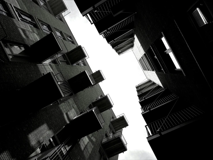 a black and white photo of a tall building, a black and white photo, by Jacob Toorenvliet, balconies, sky view, location [ chicago ( alley ) ], terrified