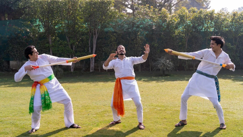 a group of men standing on top of a lush green field, an album cover, inspired by Bapu, pexels contest winner, samikshavad, practising sword stances, three head one body, white, holiday season