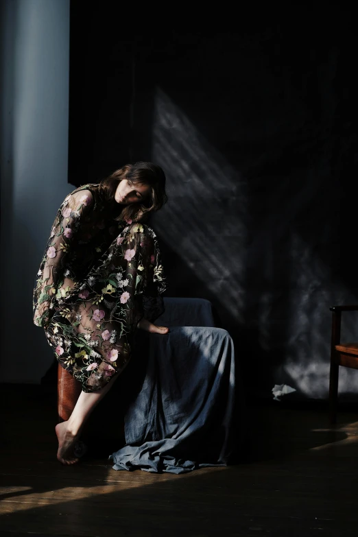 a woman leaning against a chair in a dark room, inspired by Anna Füssli, baroque, floral dream, sheer fabrics, crawling out of a dark room, on a gray background