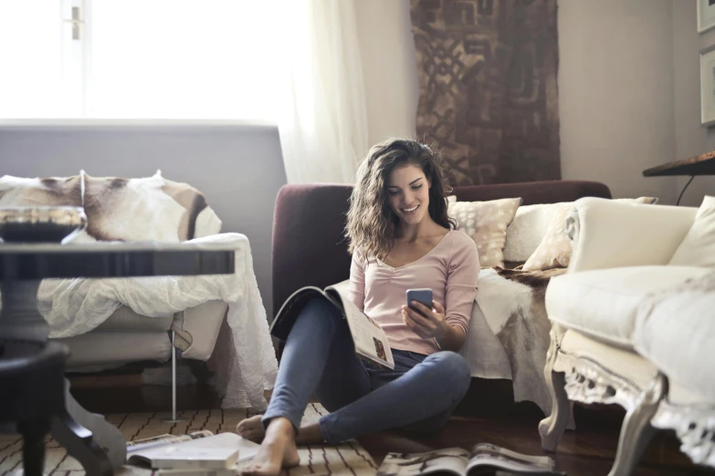 a woman sitting on the floor using a cell phone, reading the book about love, sitting across the room, australian, integrating with technology