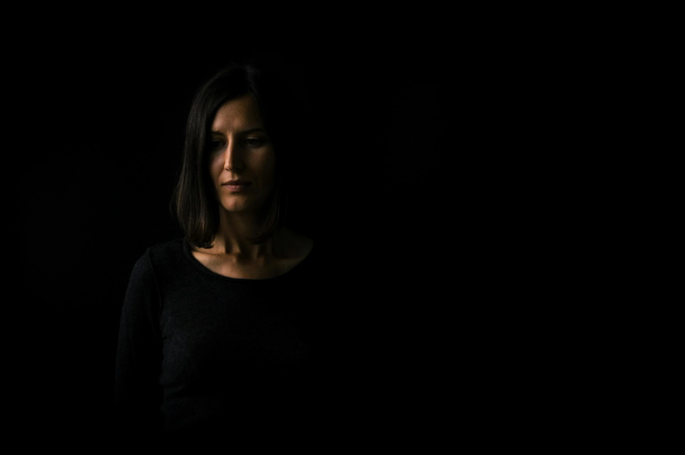 a woman standing in front of a black background, an album cover, by Giuseppe Avanzi, unsplash, portrait casting long shadows, 40 years old women, journalism photo, group of people in a dark room