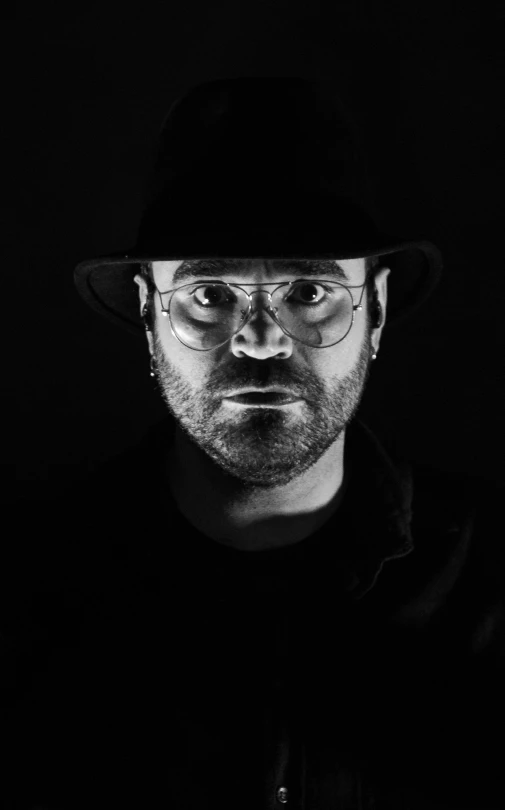 a black and white photo of a man in a hat and glasses, a black and white photo, pexels, conceptual art, style of rafael pavarotti, vantablack gi, studio potrait, rusty