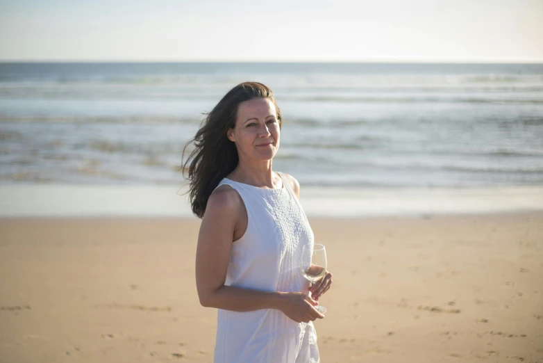 a woman standing on a beach holding a glass of wine, inspired by Zoë Mozert, happening, profile image, portrait image, a beautiful woman in white, portrait mode photo