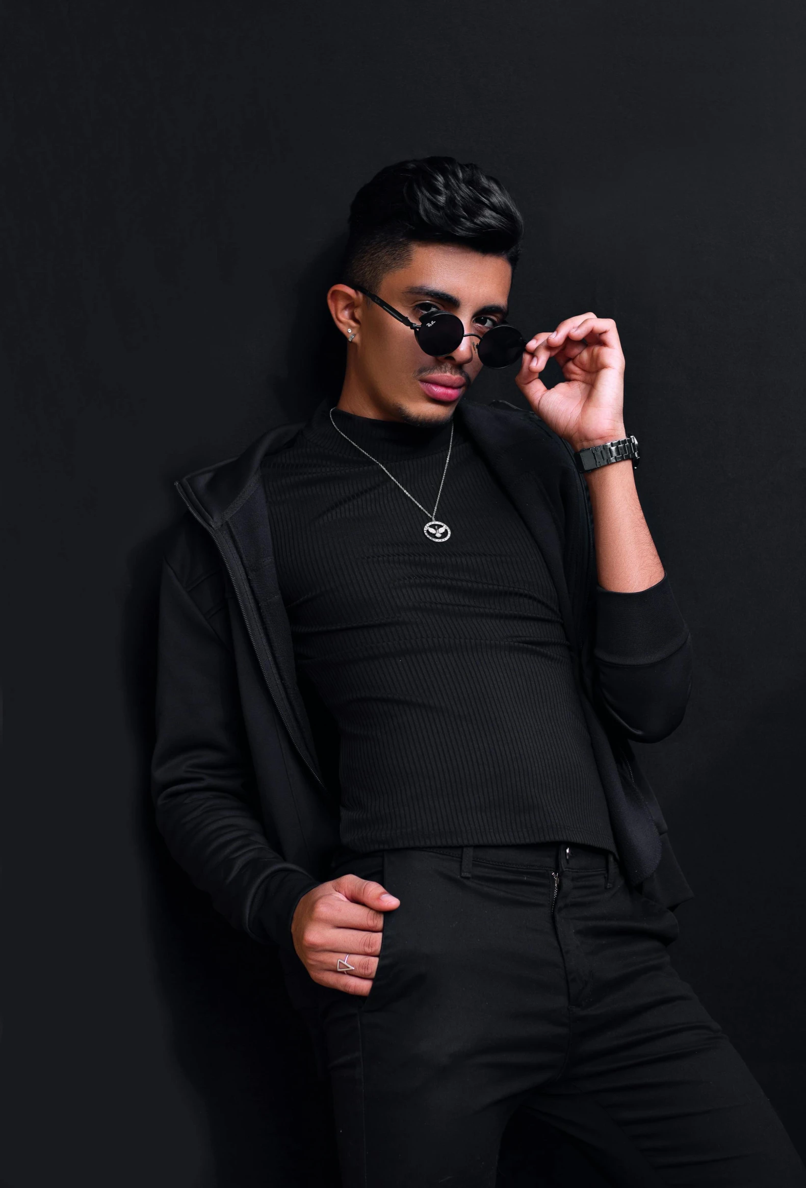 a man standing in front of a black wall, inspired by Randy Vargas, trending on pexels, rapper bling jewelry, wearing black tight clothing, with sunglass, male teenager