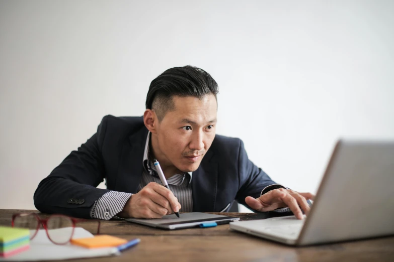 a man sitting at a desk in front of a laptop computer, a portrait, by Simon Gaon, unsplash, shin hanga, multiple stories, holding pencil, ethnicity : japanese, serious business