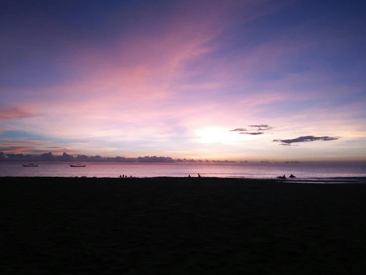 a group of people standing on top of a sandy beach, by Robbie Trevino, pexels contest winner, minimalism, purple sunset, manila, which shows a beach at sunset, photo of the middle of the ocean