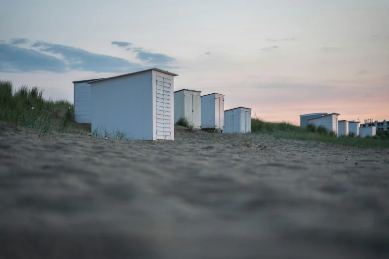 a row of beach huts sitting on top of a sandy beach, unsplash contest winner, photorealism, late summer evening, white buildings, bunkers, ignant