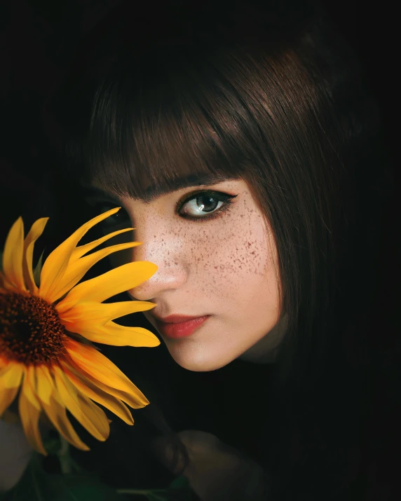 a woman holding a sunflower in front of her face, inspired by Elsa Bleda, trending on pexels, brown hair and large eyes, with freckles, ((photorealistic)), dark photo