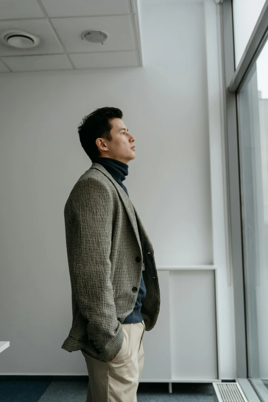 a man standing in an office looking out a window, inspired by Joong Keun Lee, unsplash, wearing a turtleneck and jacket, elegant profile pose, asian human, is tall