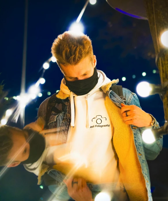 a man standing next to a woman wearing a face mask, a picture, by Adam Marczyński, trending on pexels, wearing jeans and a black hoodie, nights, a blond, wearing a yellow hoodie