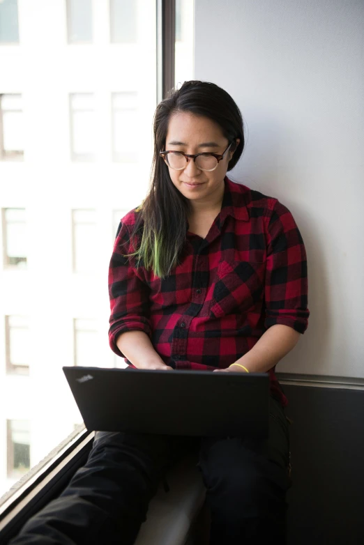 a woman sitting on a window sill using a laptop, inspired by Ruth Jên, happening, wearing a flannel shirt, eric hu, developers, wearing black rimmed glasses