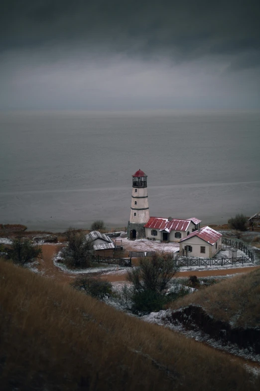 a lighthouse sitting on top of a hill next to a body of water, near lake baikal, on a dark winter's day, red roofs, low quality photo