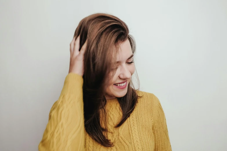 a woman in a yellow sweater combing her hair, trending on pexels, hurufiyya, bronze brown hair, half onesided smile, side - view, uploaded