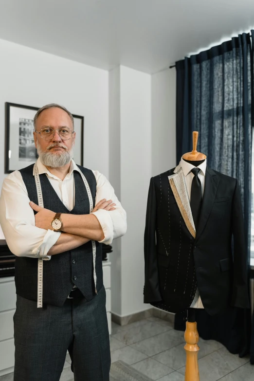 a man standing next to a mannequin in a room, wearing a suit and glasses, with a beard and a black jacket, markus vogt, wearing suit vest