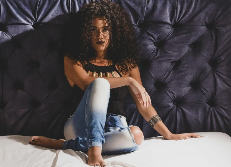 a beautiful young woman sitting on top of a bed, inspired by Esaias Boursse, pexels contest winner, antipodeans, curly black hair, jeans, middle eastern, uncropped