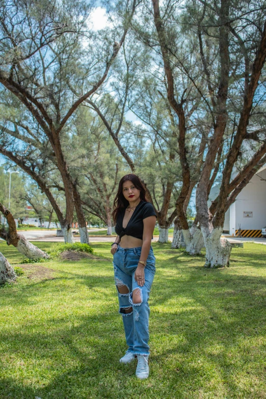 a woman standing on top of a lush green field, a picture, by Robbie Trevino, wearing jeans, in a beachfront environment, shady look, trees