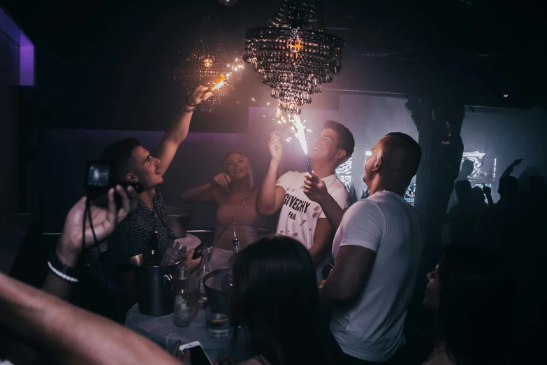 a group of people standing around a table holding sparklers, by Niko Henrichon, vip room, josh black, stars on top of the crown, max prentis