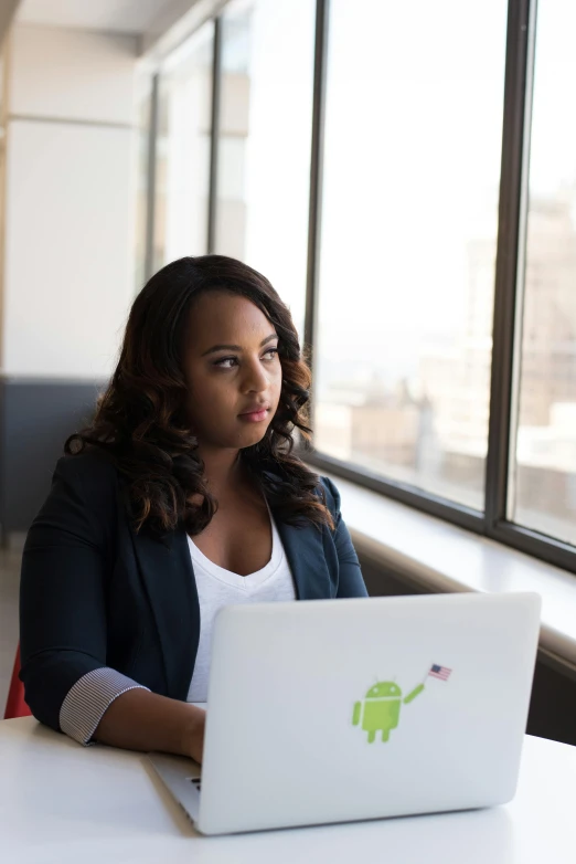 a woman sitting at a table with a laptop, by Lily Delissa Joseph, pexels contest winner, african female android, promo image, in the office, who is a male android