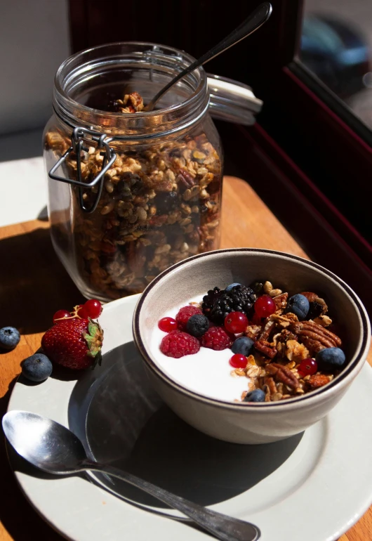 a bowl of granola sitting on top of a white plate, by Leo Michelson, pexels contest winner, bright sunlight, jars, dwell, oaks