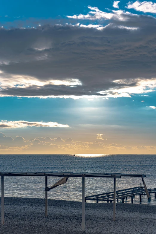 a couple of benches sitting on top of a sandy beach, sun shining through clouds, manly, viewed from the ocean, sun set