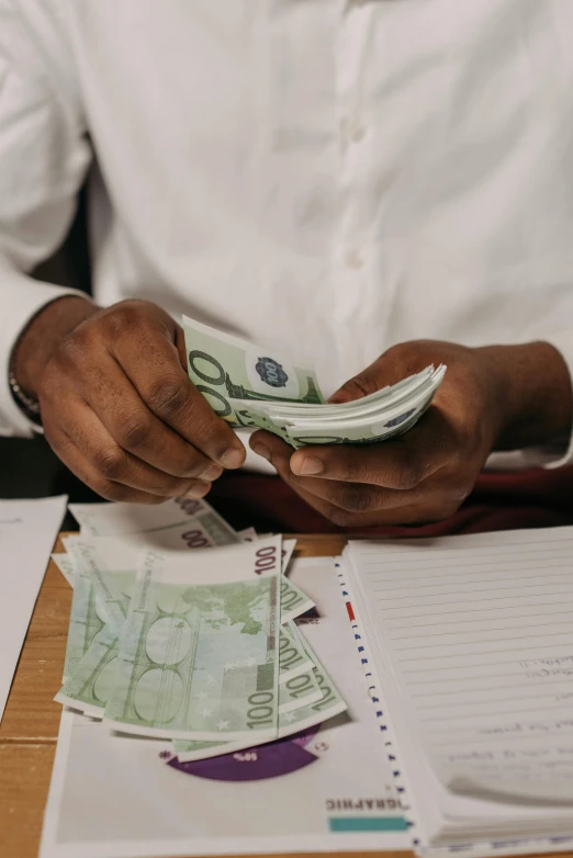 a man sitting at a desk holding a stack of money, by Matija Jama, pexels contest winner, renaissance, aida muluneh, thumbnail, small in size, promo image