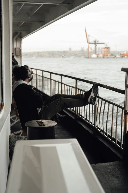 a man sitting on a boat looking out at the water, 🚿🗝📝, on the deck of a ship, istanbul, grey