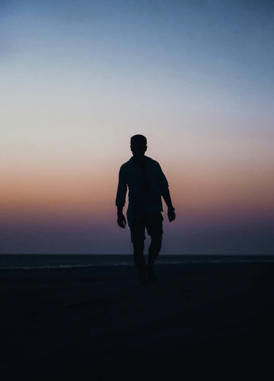 a man standing on top of a beach next to the ocean, pexels, happening, character silhouette, walking to the right, profile image, predawn