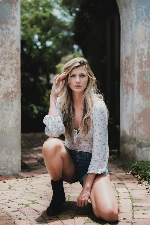 a woman squatting on a brick walkway, a portrait, by Carey Morris, trending on unsplash, renaissance, with long blond hair, dressed in a top and shorts, country style, in front of white back drop