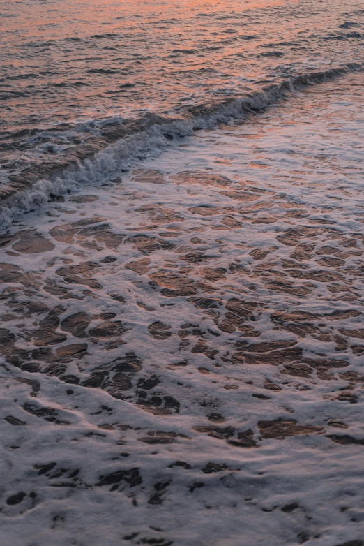 a man standing on top of a beach next to the ocean, an album cover, inspired by Elsa Bleda, unsplash, water ripples, soft light 4 k in pink, detail shot, late evening