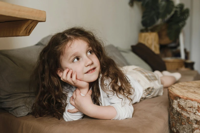 a little girl laying on top of a bed, pexels contest winner, happening, brown curly hair, sitting on a couch, looking to his side, thumbnail