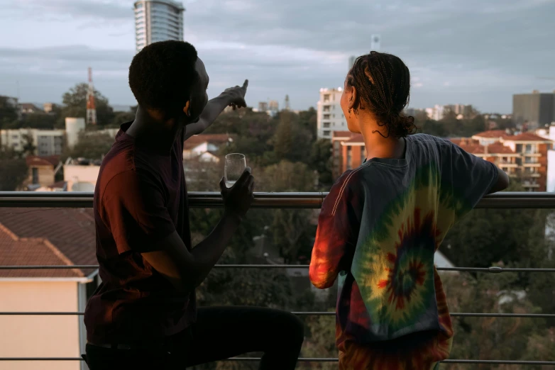a couple of people standing on top of a balcony, by Ella Guru, pexels contest winner, happening, tie die shirt, unmistakably kenyan, drinking and smoking, aboriginal australian hipster