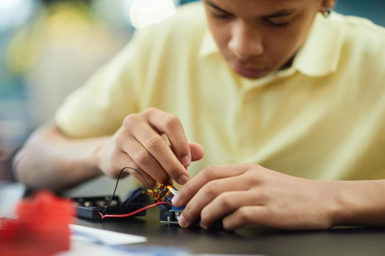 a boy is working on an electronic device, pexels, process art, sustainable materials, teaser, schools, darren quach