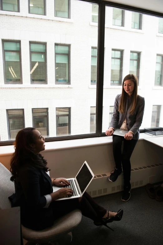 a couple of women sitting next to each other in front of a window, happening, office ceiling panels, using a macbook, standing, multiple stories