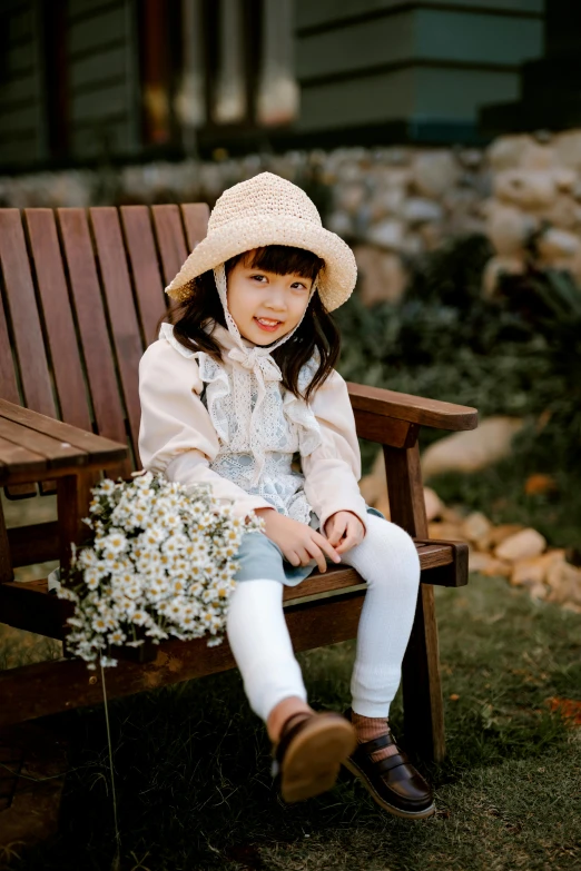 a little girl sitting on top of a wooden bench, white straw flat brimmed hat, li zixin, wearing a hoodie and flowers, sitting on an armchair