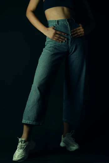 a woman standing in the dark with her hands on her hips, pexels contest winner, photorealism, tight blue jeans and cool shoes, studio medium format photograph, desaturated color, large pants