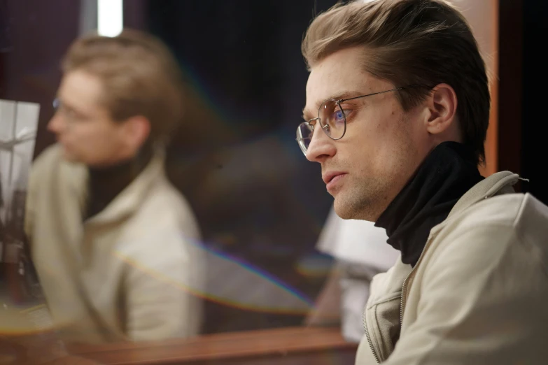 a man with glasses sitting in front of a mirror, a colorized photo, inspired by Oskar Lüthy, reddit, in an arena in movie dune-2021, high society, brad pitt is leon s. kennedy, he is wearing a trenchcoat