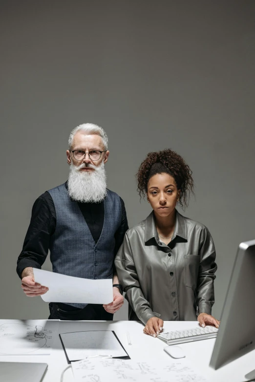 a man and a woman standing in front of a computer, by Adam Marczyński, trending on unsplash, renaissance, some grey hair in beard, standing in class, plain background, looking serious