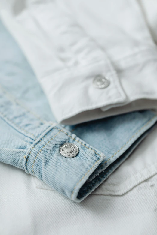 a pair of jeans laying on top of a bed, by Nina Hamnett, trending on unsplash, button up shirt, silver，ivory, pale blue, badge on collar