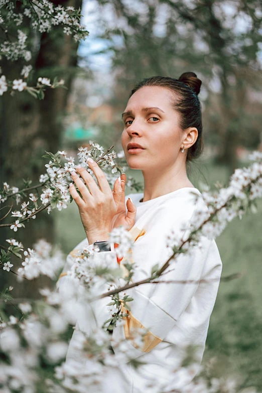 a woman standing in front of a tree with white flowers, by Adam Marczyński, pexels contest winner, renaissance, anjali mudra, dafne keen, wearing a hoodie and flowers, ukrainian monk
