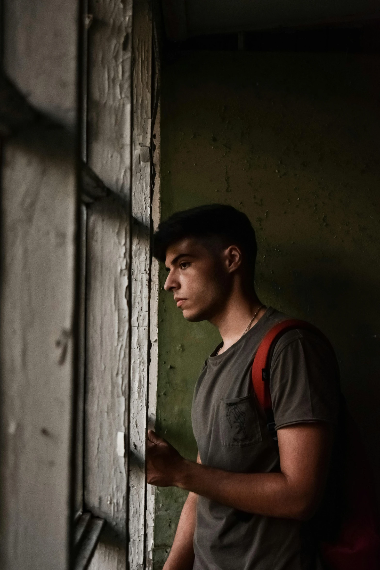 a man with a backpack looking out of a window, a picture, pexels contest winner, portrait of a rugged young man, in a dark warehouse, color photo, ( ( theatrical ) )