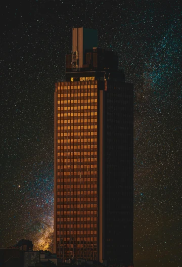 a tall building in the middle of a city at night, unsplash contest winner, brutalism, stars and planets visible, hannover, gold, hyper - detailed color photo