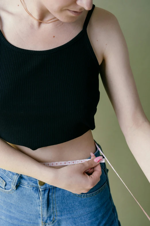 a woman measuring her waist with a tape, a colorized photo, by Nicolette Macnamara, trending on pexels, square jaw-line, wearing a cropped top, plain background, background image