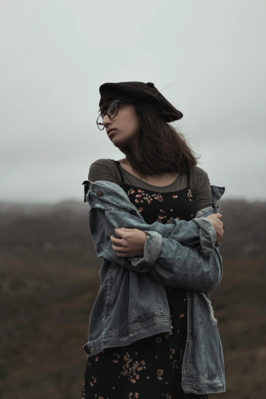 a woman standing in the middle of a field, trending on pexels, gray skin. grunge, beret and sunglasses, wearing a jeans jackets, overcast mood