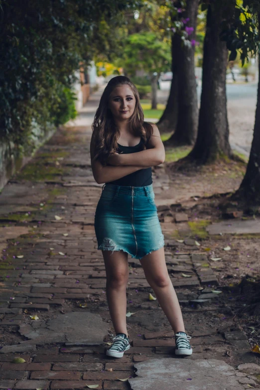 a woman standing on a sidewalk with her arms crossed, by Felipe Seade, pexels contest winner, wearing crop top and miniskirt, young southern woman, avatar image, dressed in a worn