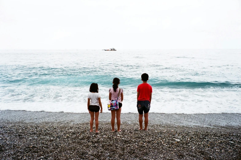 a group of people standing on top of a beach next to the ocean, inspired by Thomas Struth, pexels contest winner, hyperrealism, kids, threes, traveling in france, taiwan